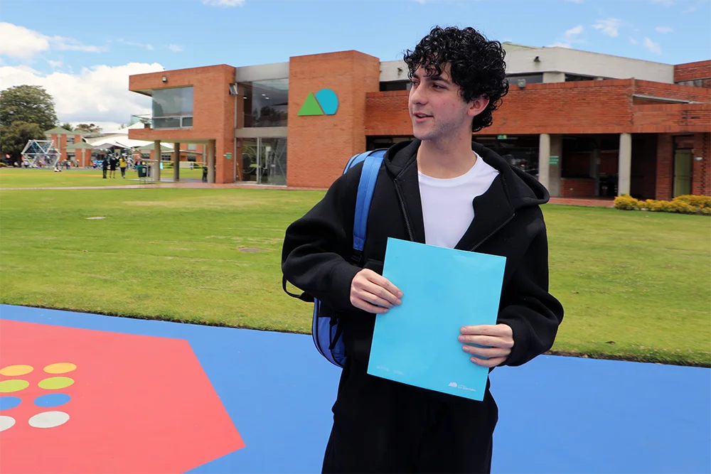 Estudiante de bachillerato sostiene sus trabajos en el campus del Gimnasio La Montaña